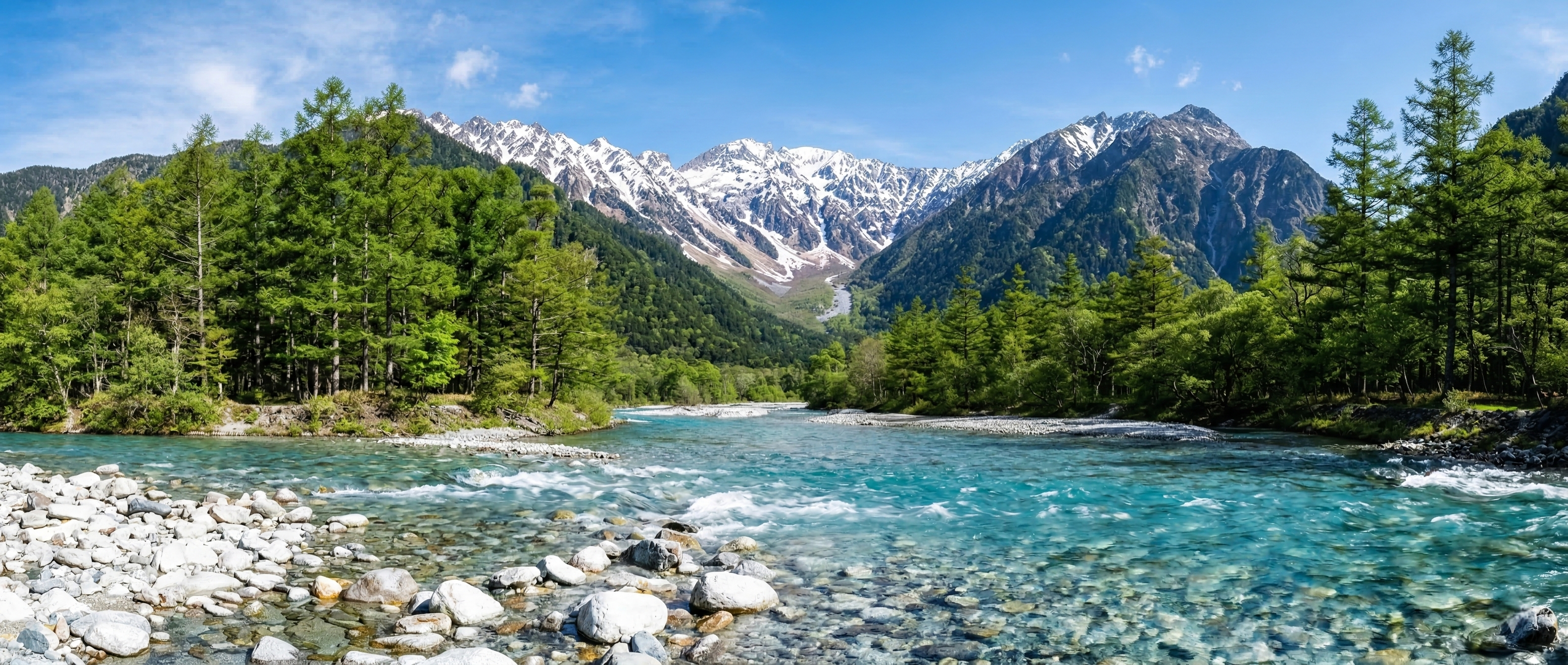 A wide panoramic view of the turquoise Azusa River flowing through a lush valley toward the snow-capped, jagged granite peaks of Mount Hotaka under a clear blue sky.