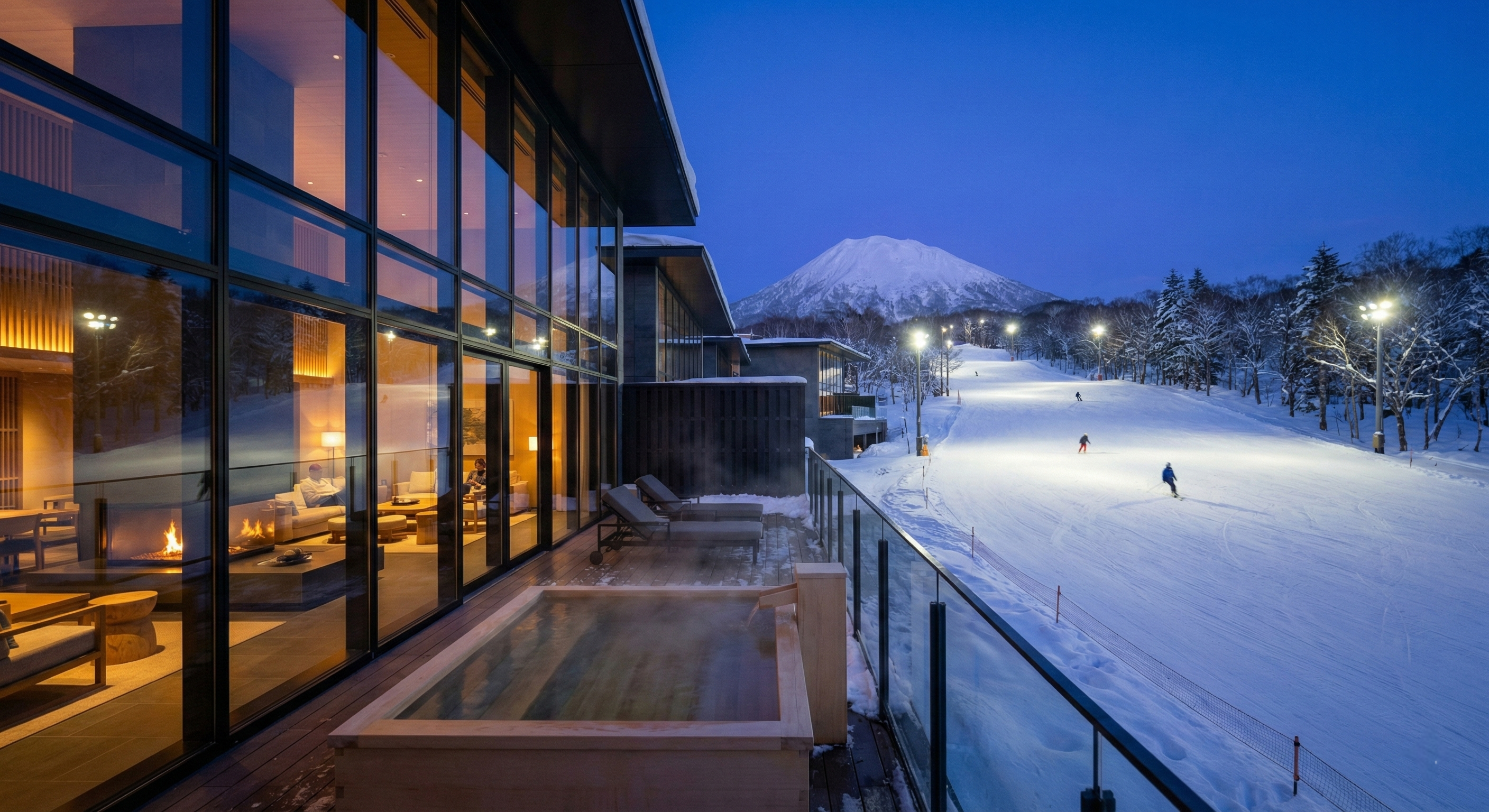 A luxurious, modern ski-in/ski-out resort in Niseko at twilight, featuring large glass windows, a private hot tub, and a direct view of an illuminated ski slope.